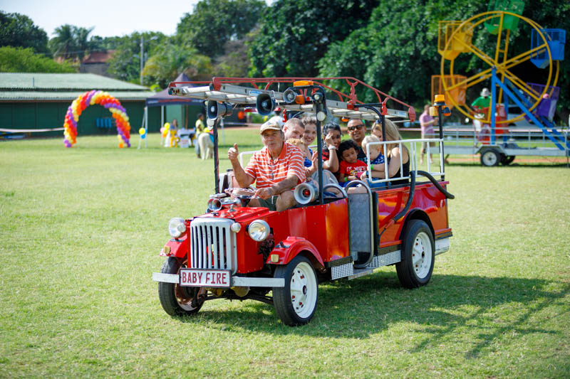 Guests riding in a fun, red vehicle on a grassy area.