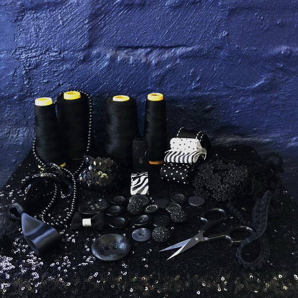 Spools of black thread, decorations, and scissors arranged on a dark surface