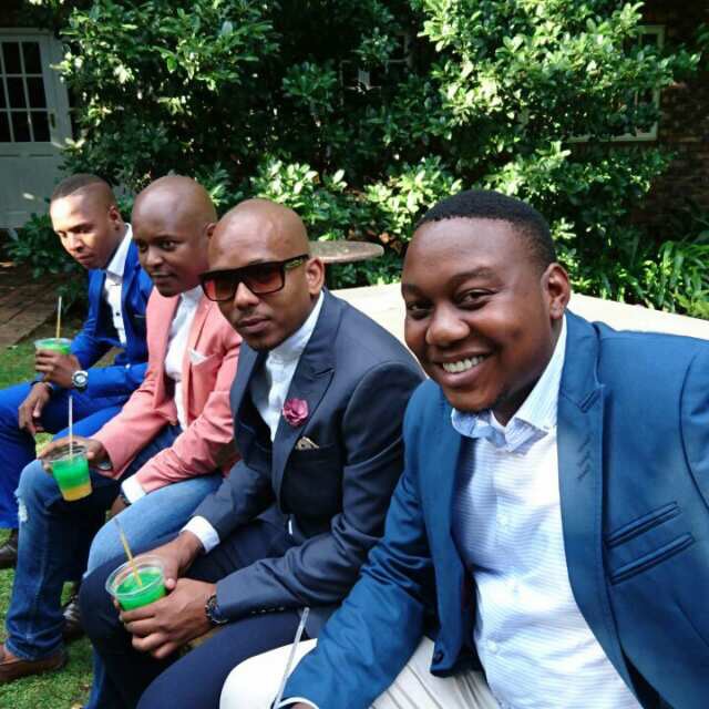 Four men in suits with drinks at an outdoor gathering