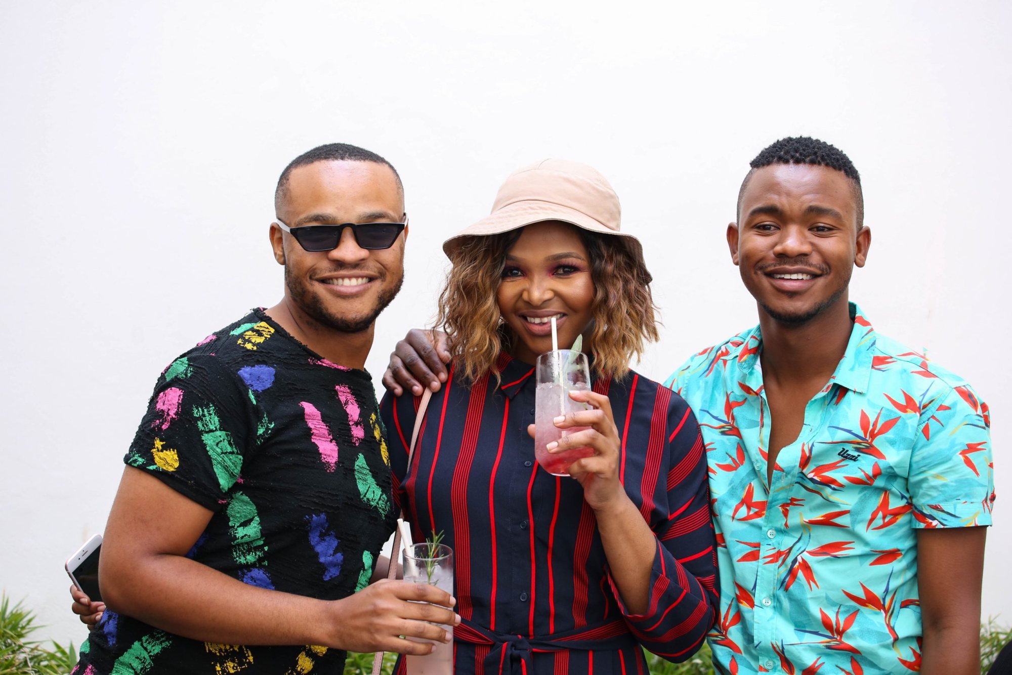 Three friends smiling and holding cocktails in a festive setting.