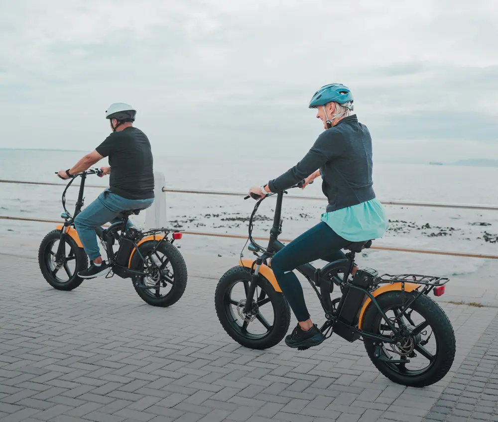 Two people riding electric bicycles along a coastal pathway.