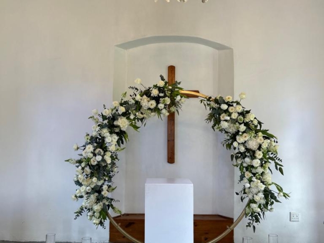 Floral arch with white flowers and a wooden cross backdrop