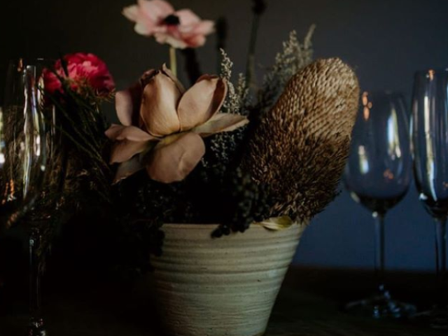 Floral centerpiece with various blooms in a pot and glassware nearby.