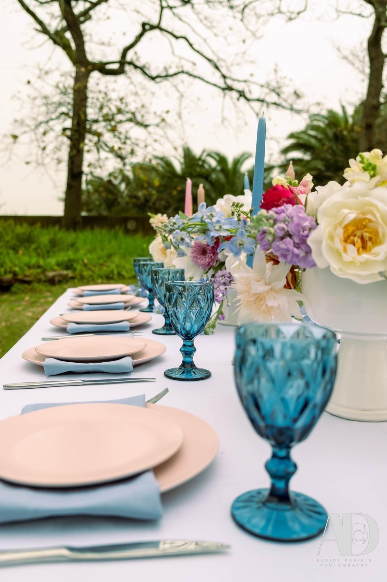 Table with pastel plates and blue glassware adorned with flowers.