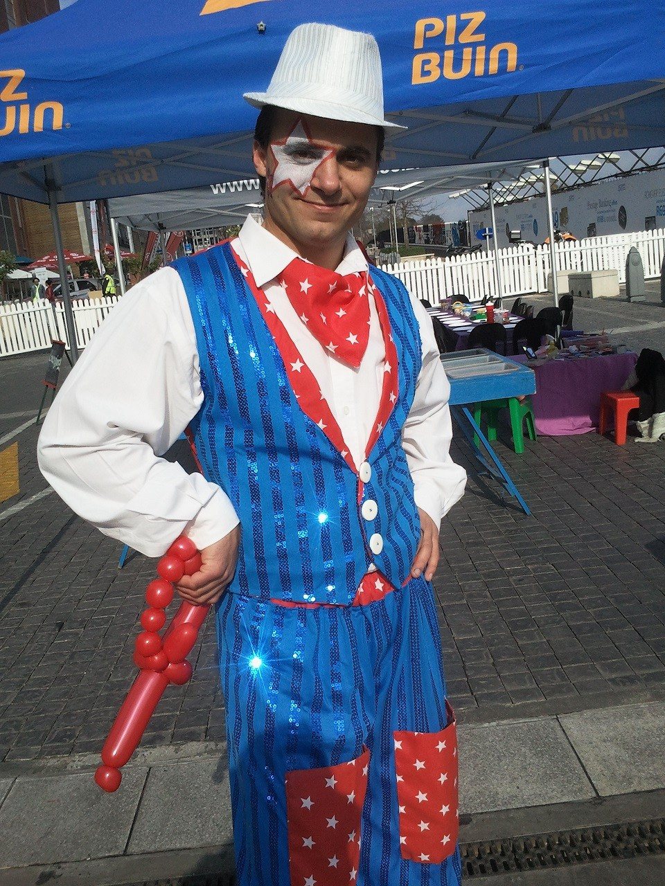 A balloon twister in colorful attire holding a balloon figure.