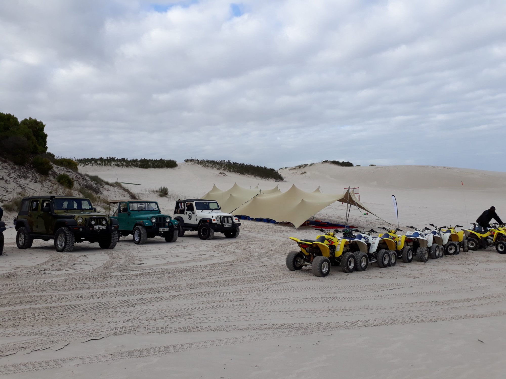 Setup of stretch tents with vehicles in sandy outdoor area