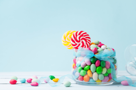 A jar filled with colorful candies and two lollipops.
