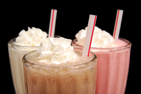Three milkshakes in clear glasses topped with whipped cream
