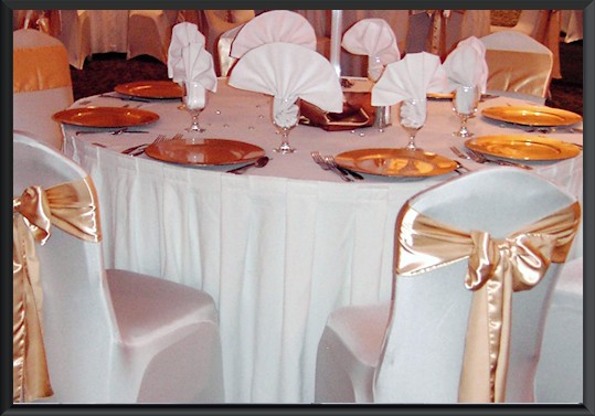 Round table with white tablecloth, gold plates, and fancy napkin folds.