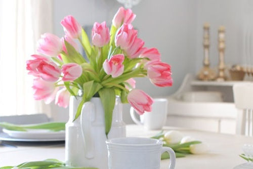 White pitcher filled with pink tulips on a dining table