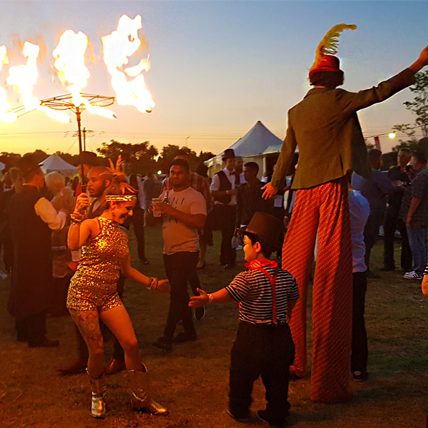 Fire dancers performing at an outdoor event with stilt walkers