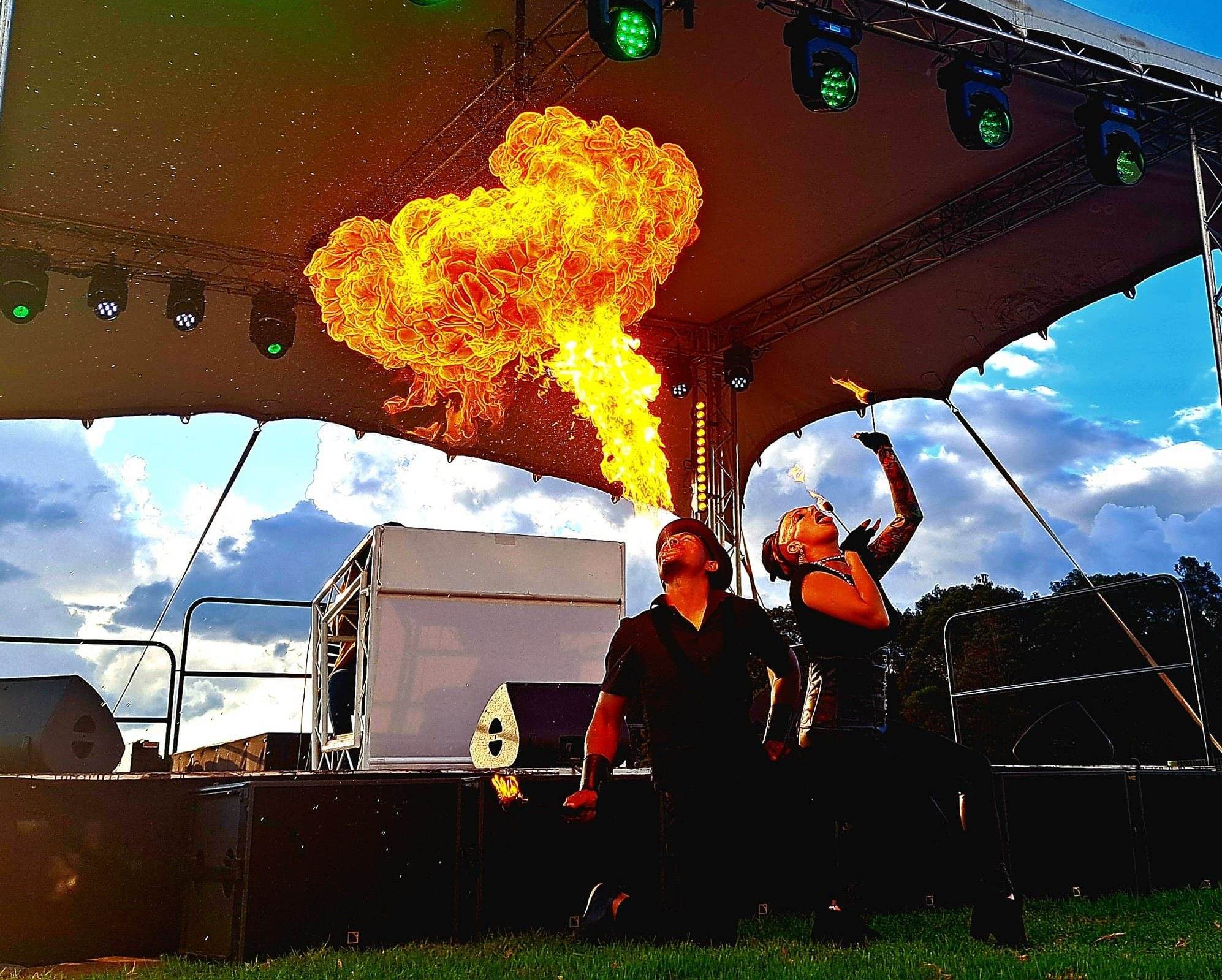 Two fire dancers performing under a large canopy with colorful lights