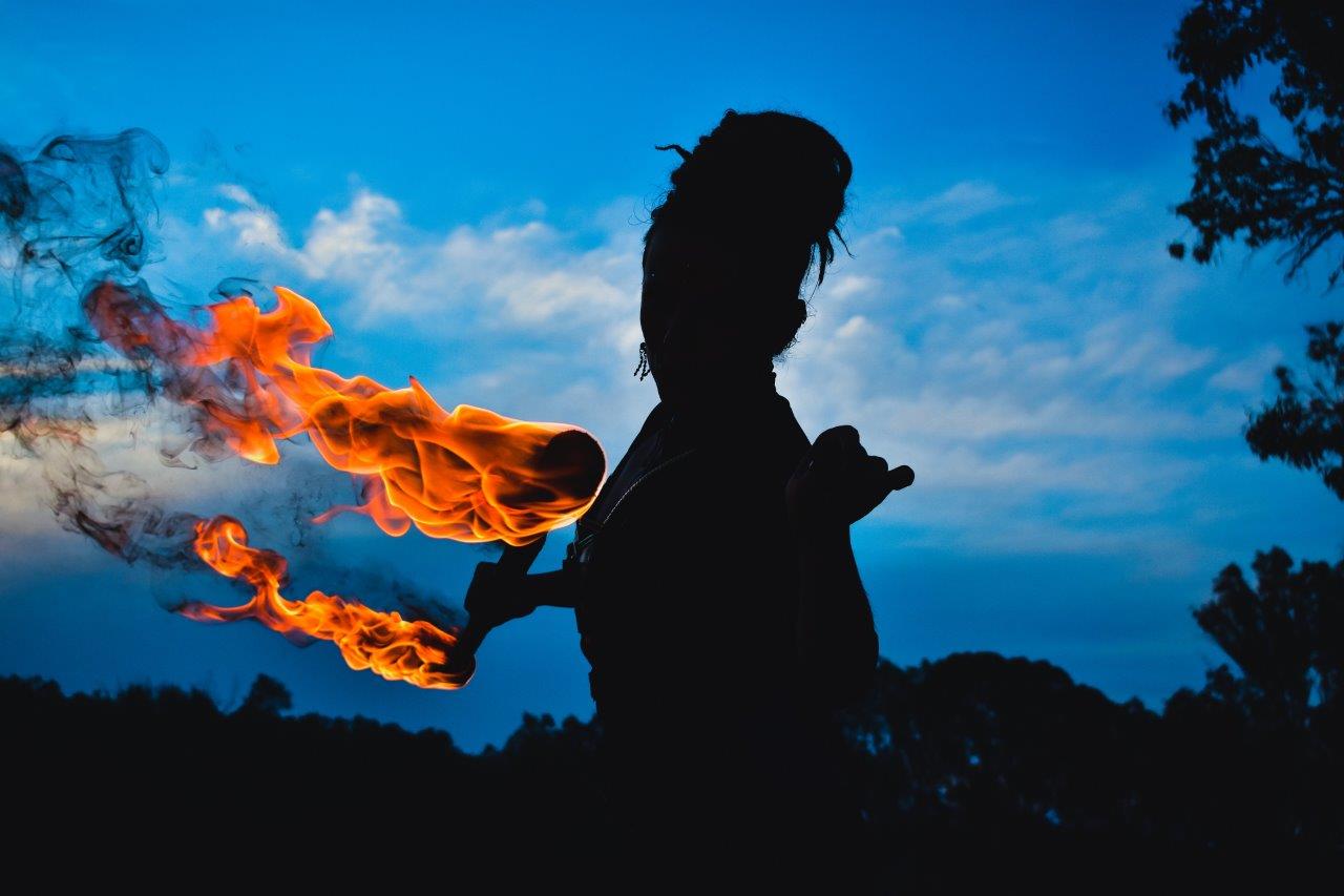 Silhouette of a fire performer capturing flames against a blue sky