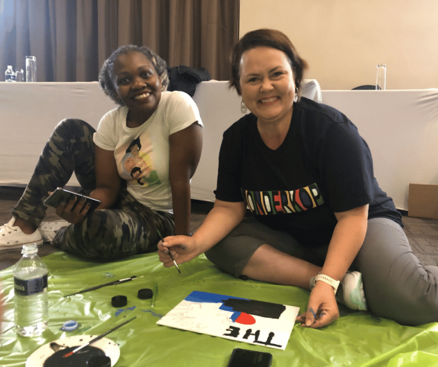 Two participants painting on a green mat during a team building event.