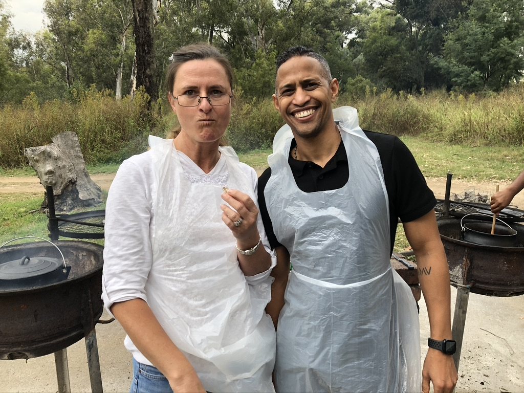 Two people engaged in a Potjiekos cooking challenge outdoors.