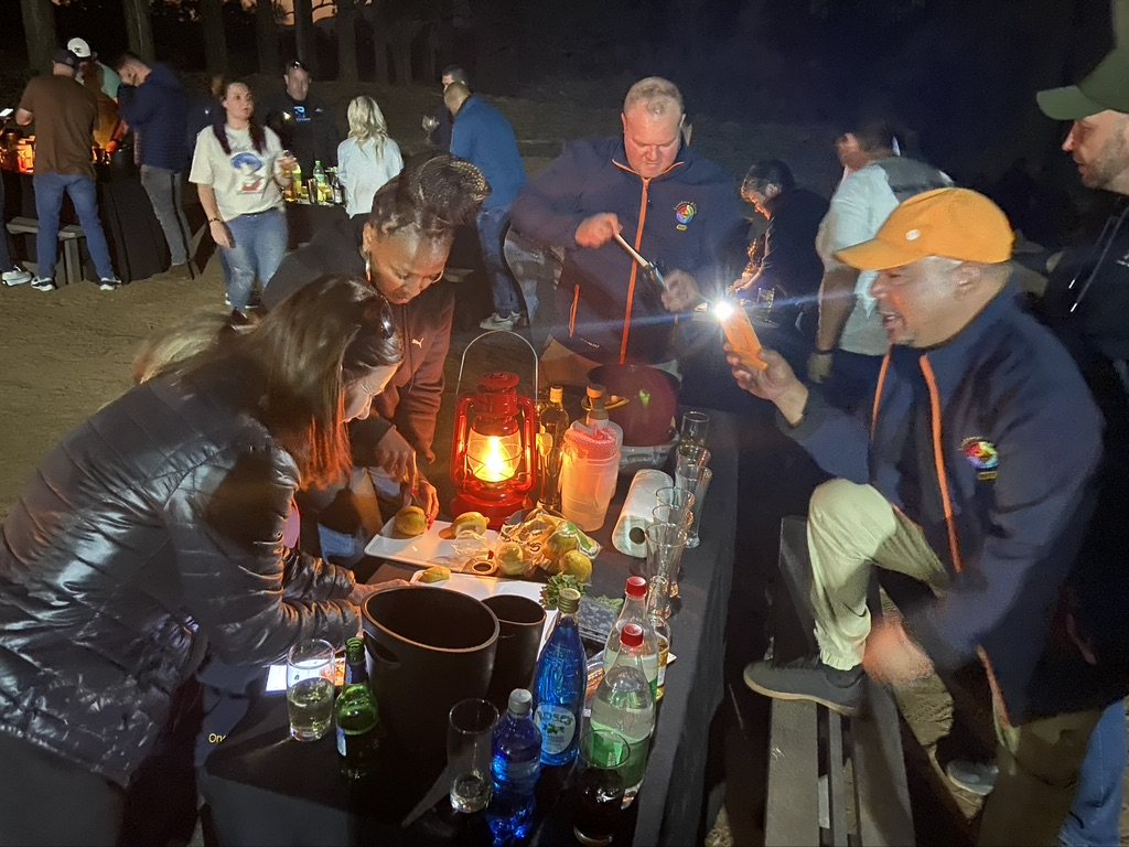Participants engage in a potjiekos cooking competition at night.