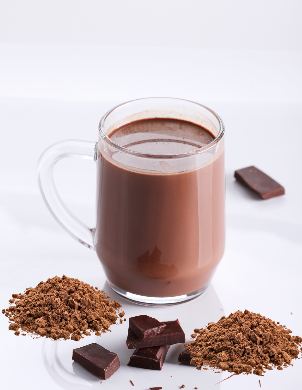 Glass mug of hot chocolate with cocoa powder and chocolate pieces.
