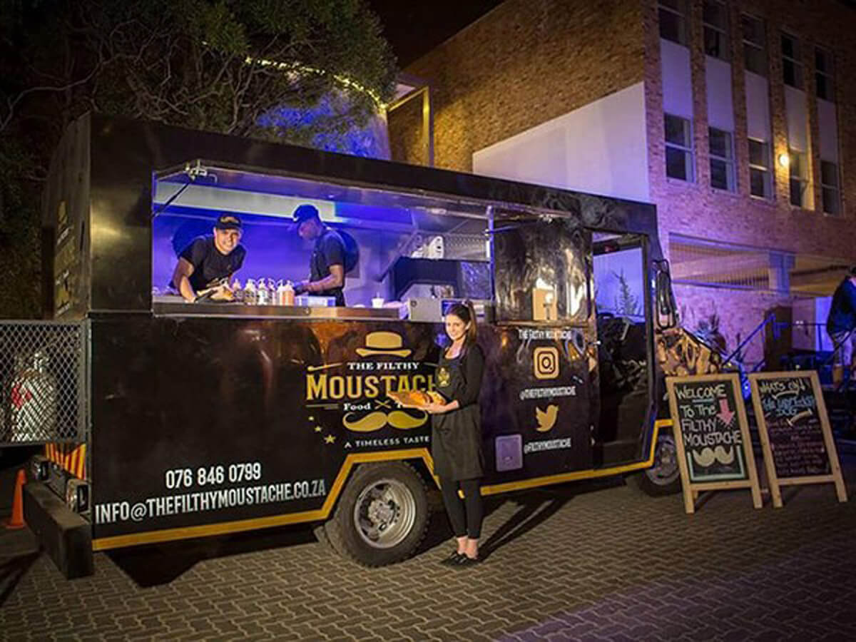 Black gourmet food truck with staff and menu display at night.