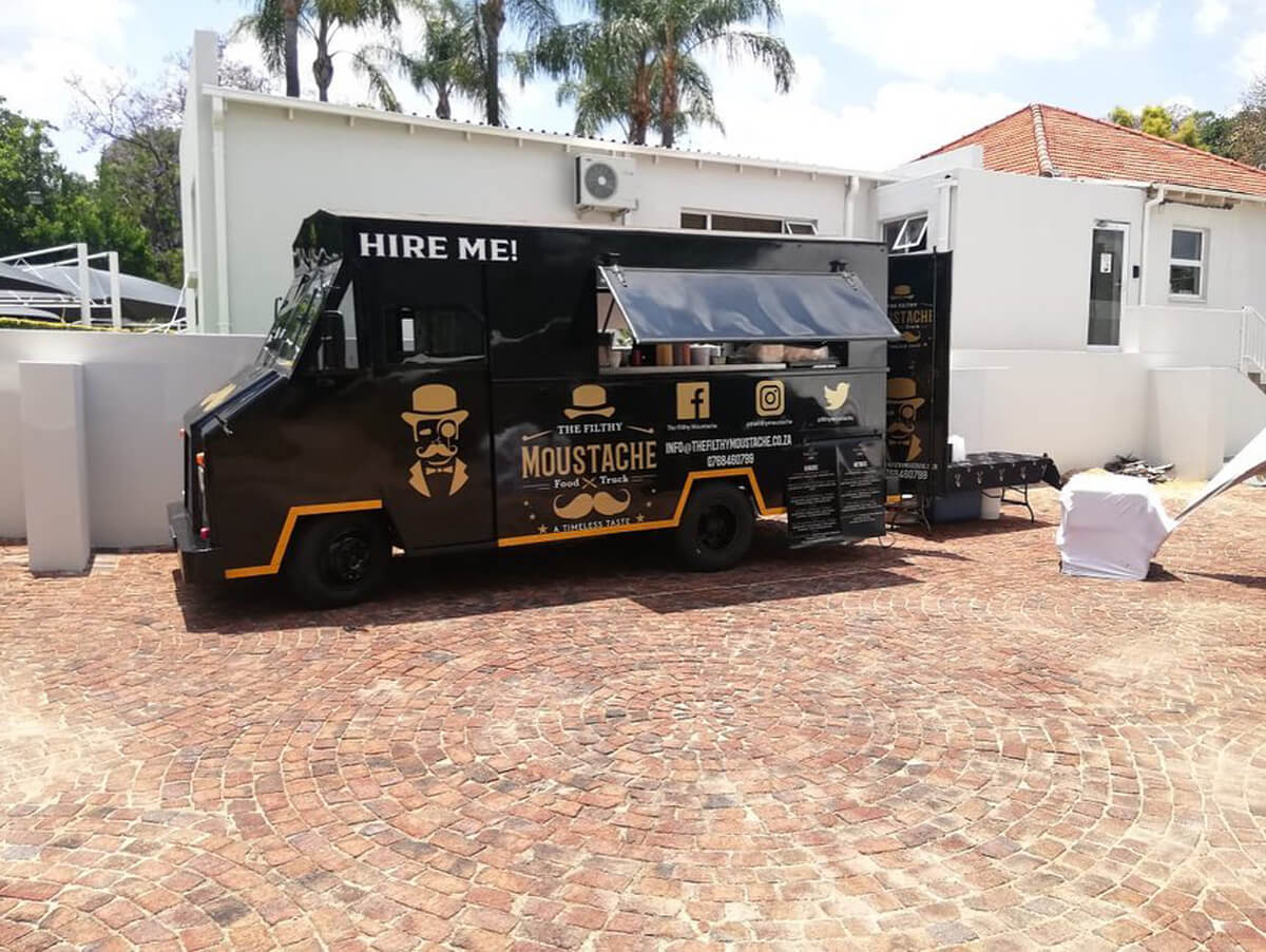 Black and yellow gourmet food truck in a paved area