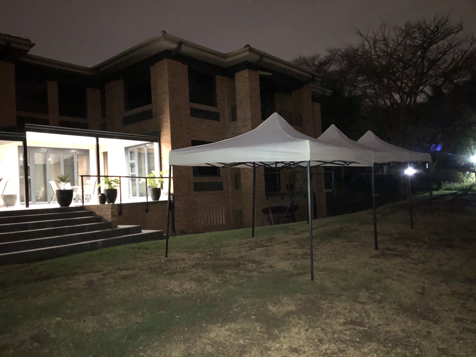 Three white gazebos set up outside a building at night.
