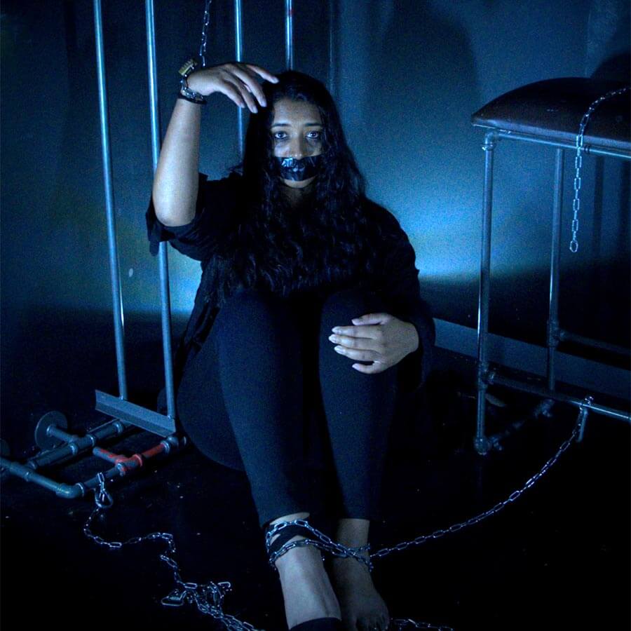 A woman in a dark escape room setting, depicting a themed scenario.