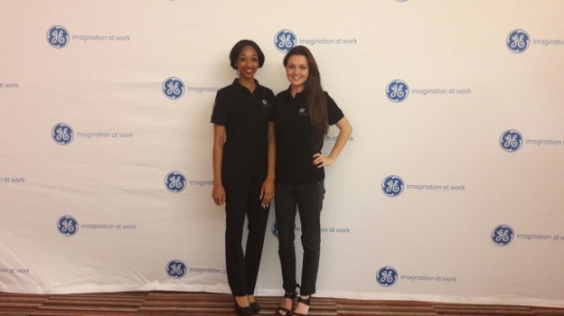 Two women in branded polo shirts standing against a backdrop