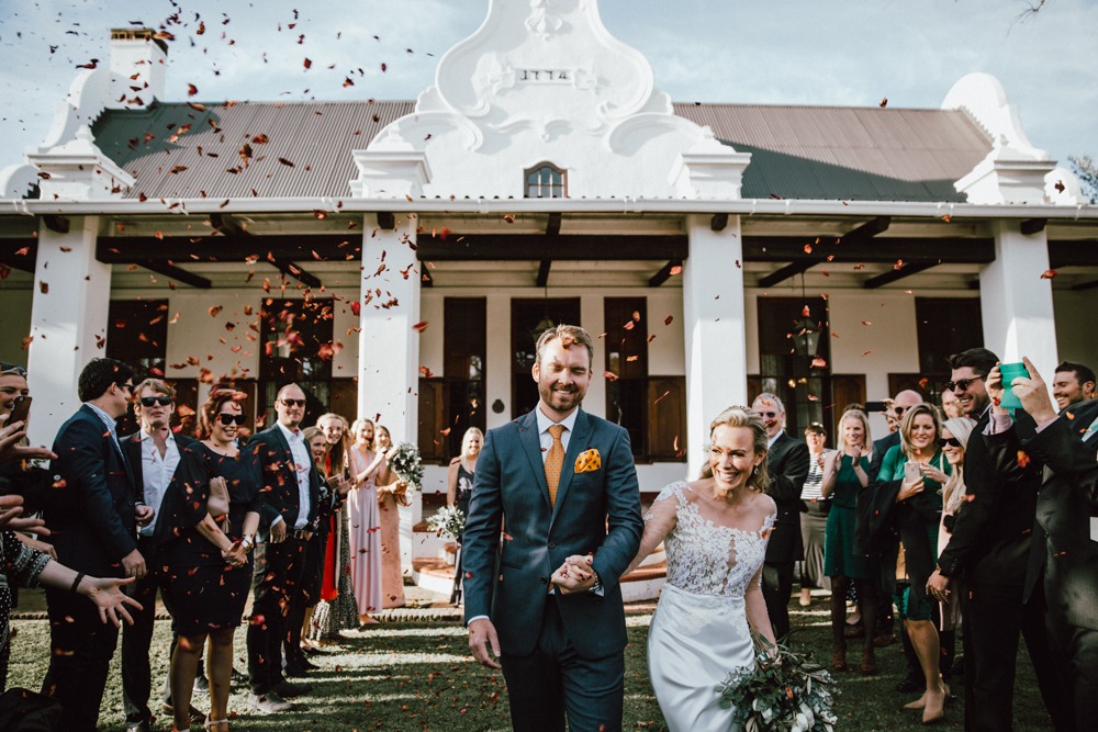 Couple walking together with guests celebrating in the background.