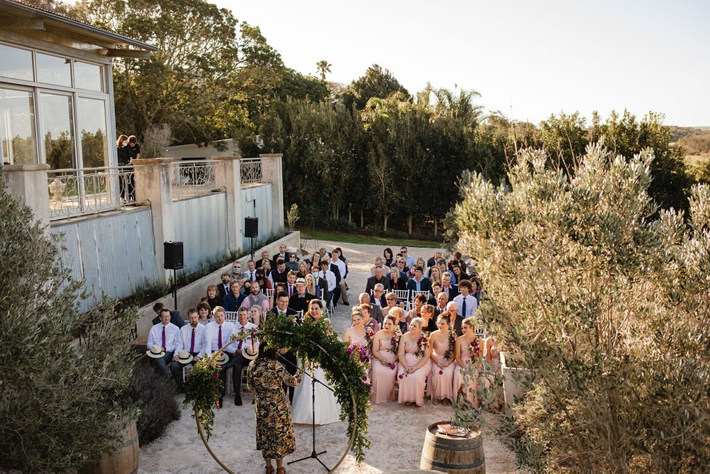 Guests at an outdoor wedding ceremony with a floral arch.