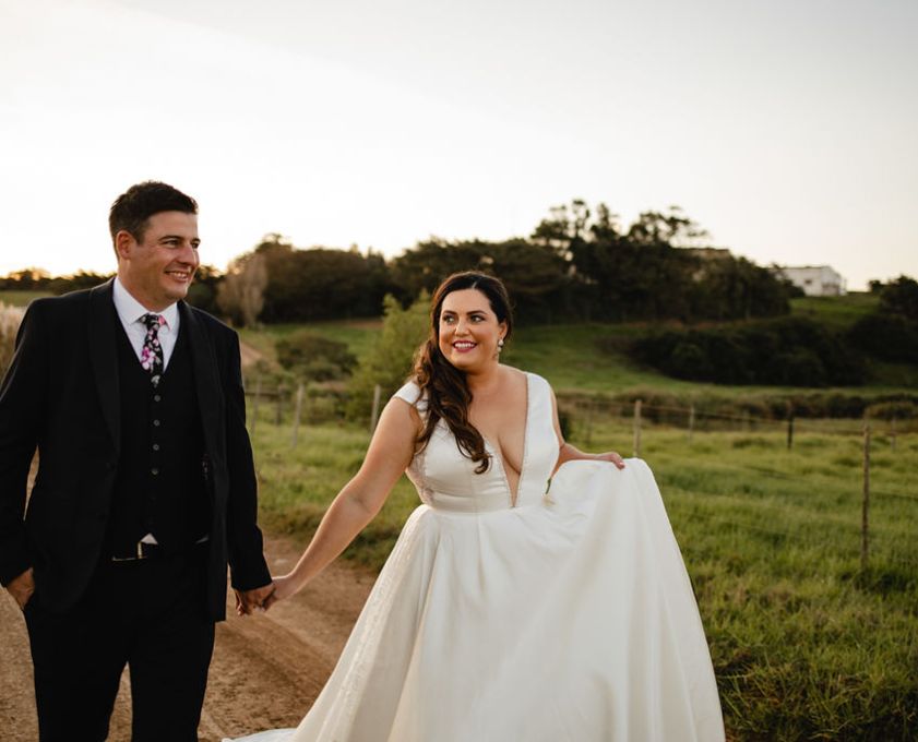 Bride and groom walking on a dirt path in a scenic landscape