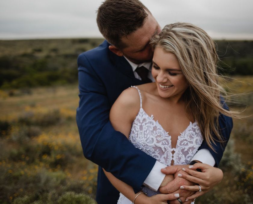 Man and woman in wedding attire embracing outdoors.
