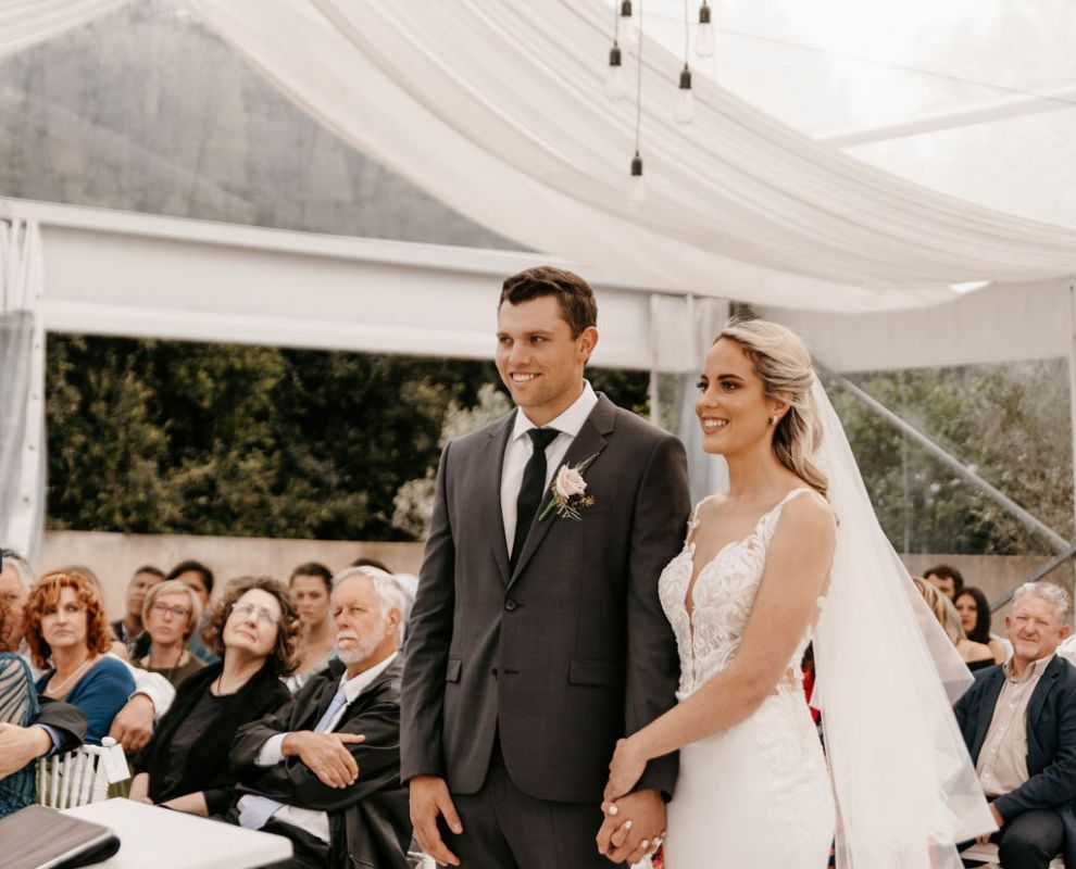 Couple holding hands at a wedding ceremony under a tent