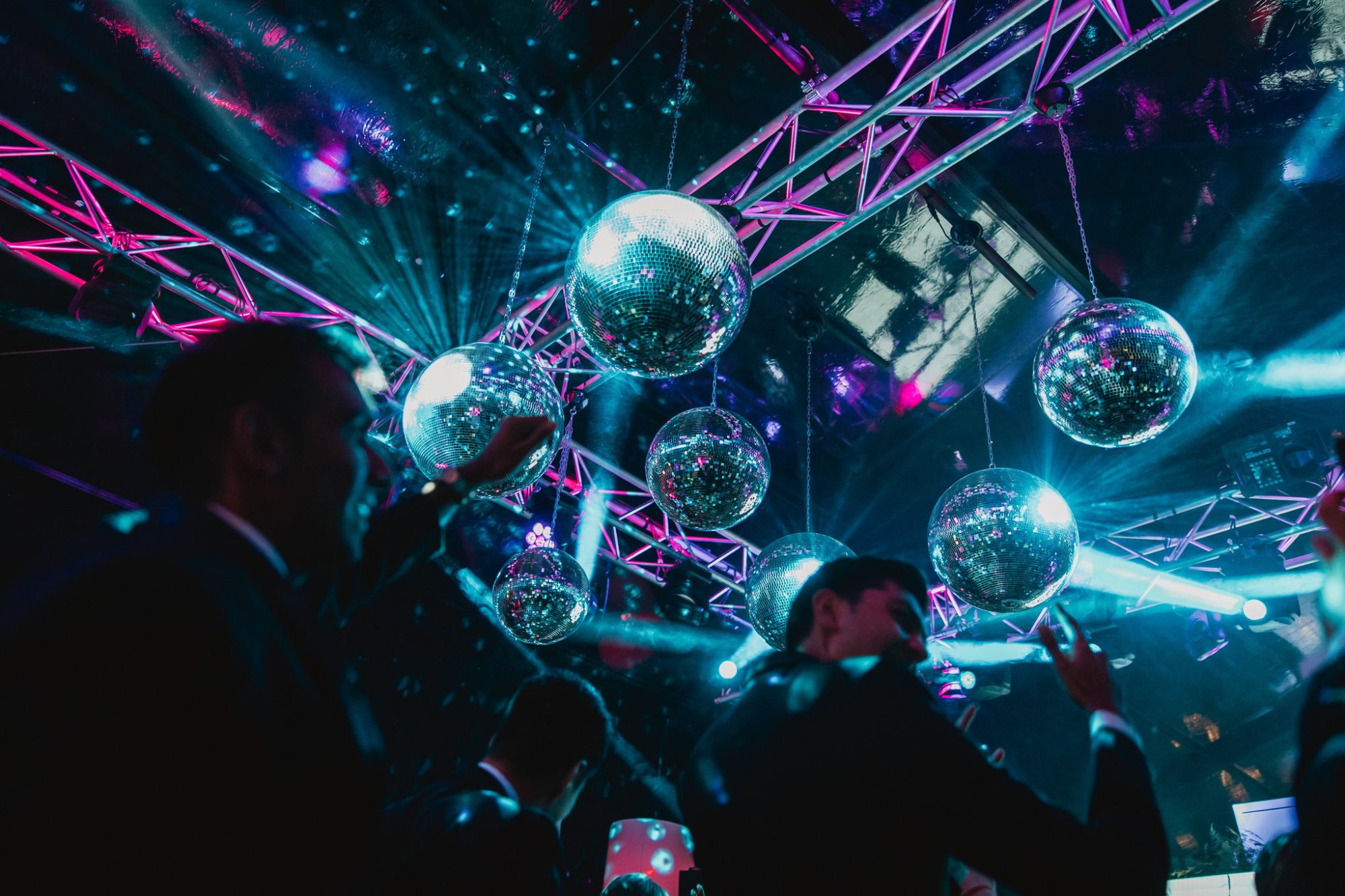 Disco balls hanging from a truss with colorful lights