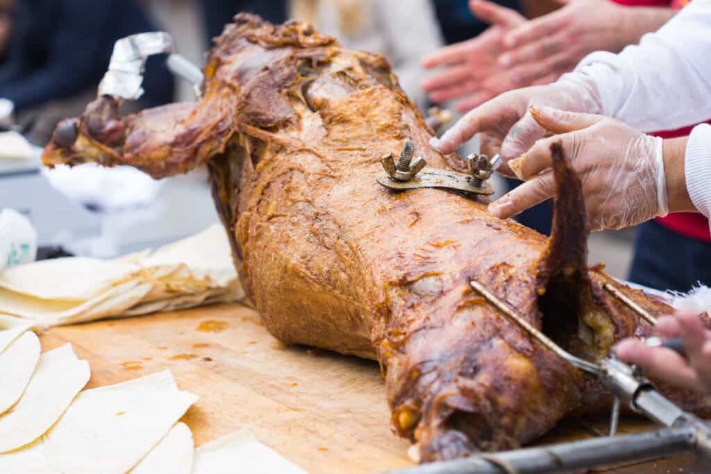 Whole lamb on a spit being carved for serving.