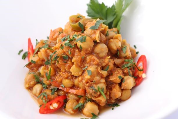 A bowl of chickpea curry garnished with herbs and chili