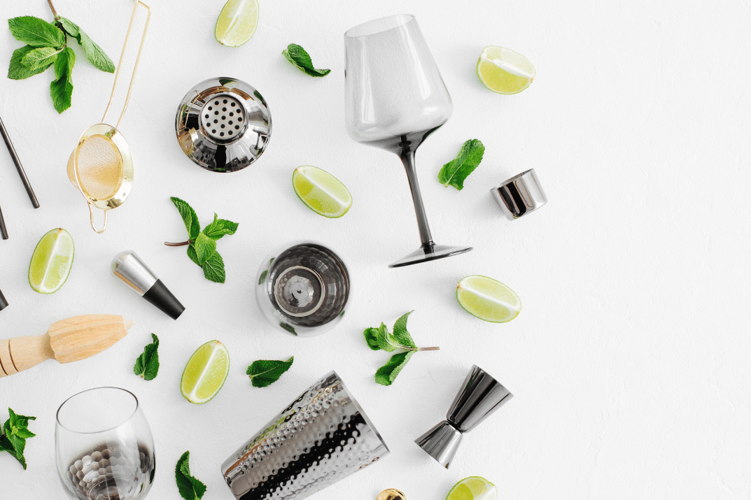 Assorted cocktail preparation tools and garnishes on a white surface.
