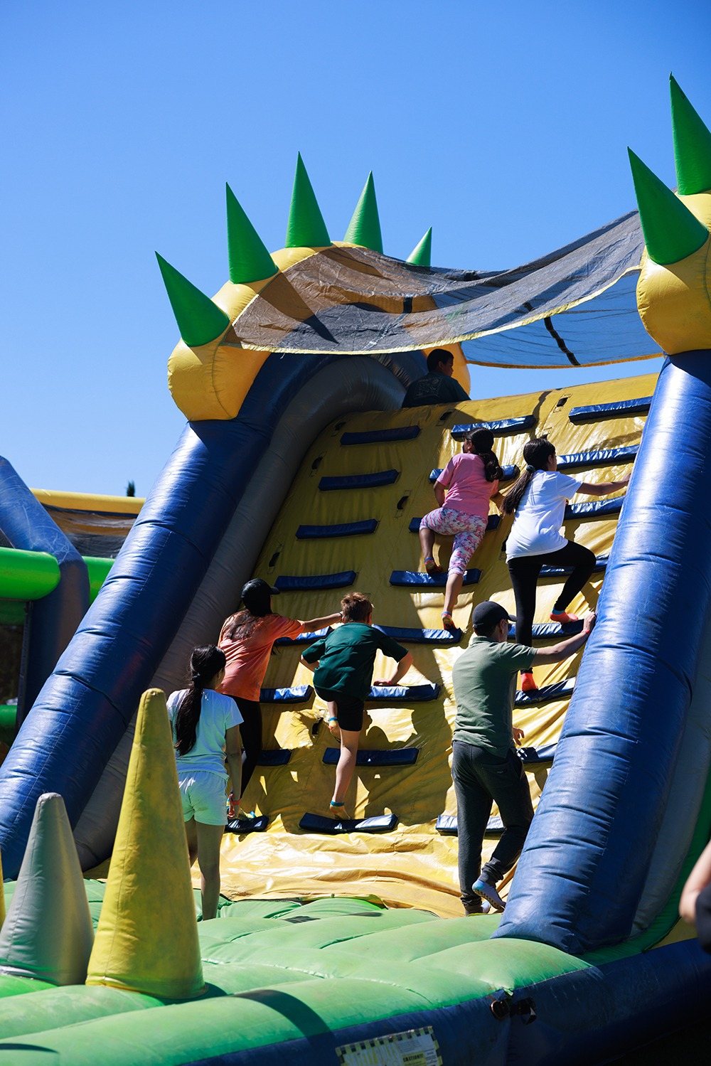 Participants climbing an inflatable obstacle wall with spikes.