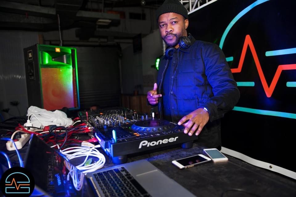 DJ performing at a console with colorful lighting.