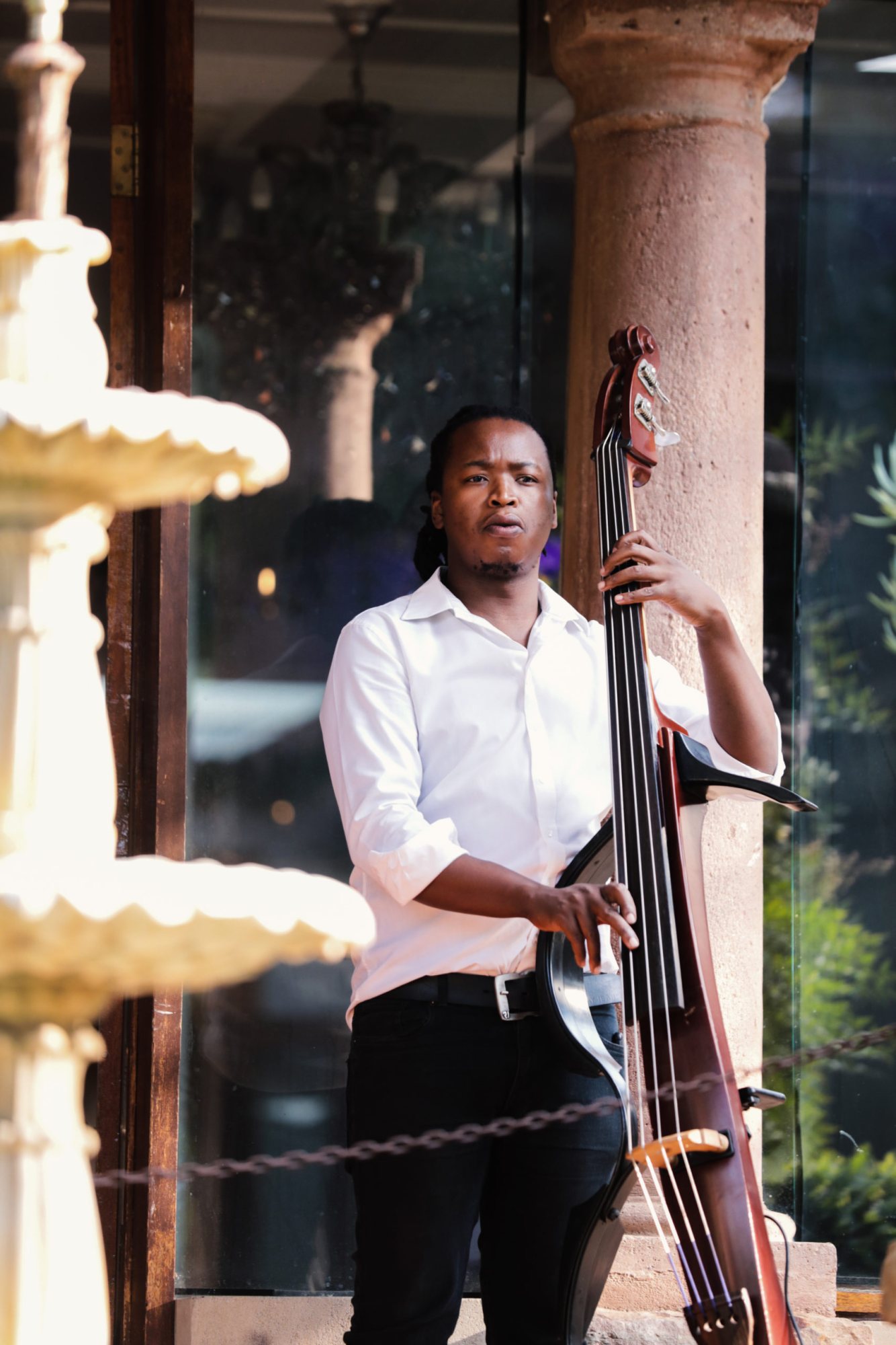 Musician in white shirt playing double bass near fountain.