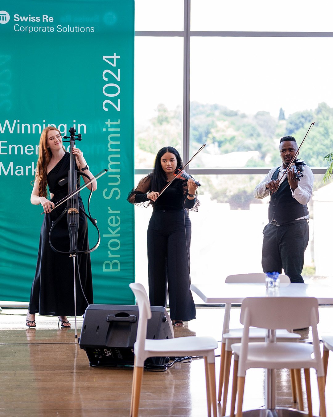 Three musicians performing with violins and cello at a corporate event.