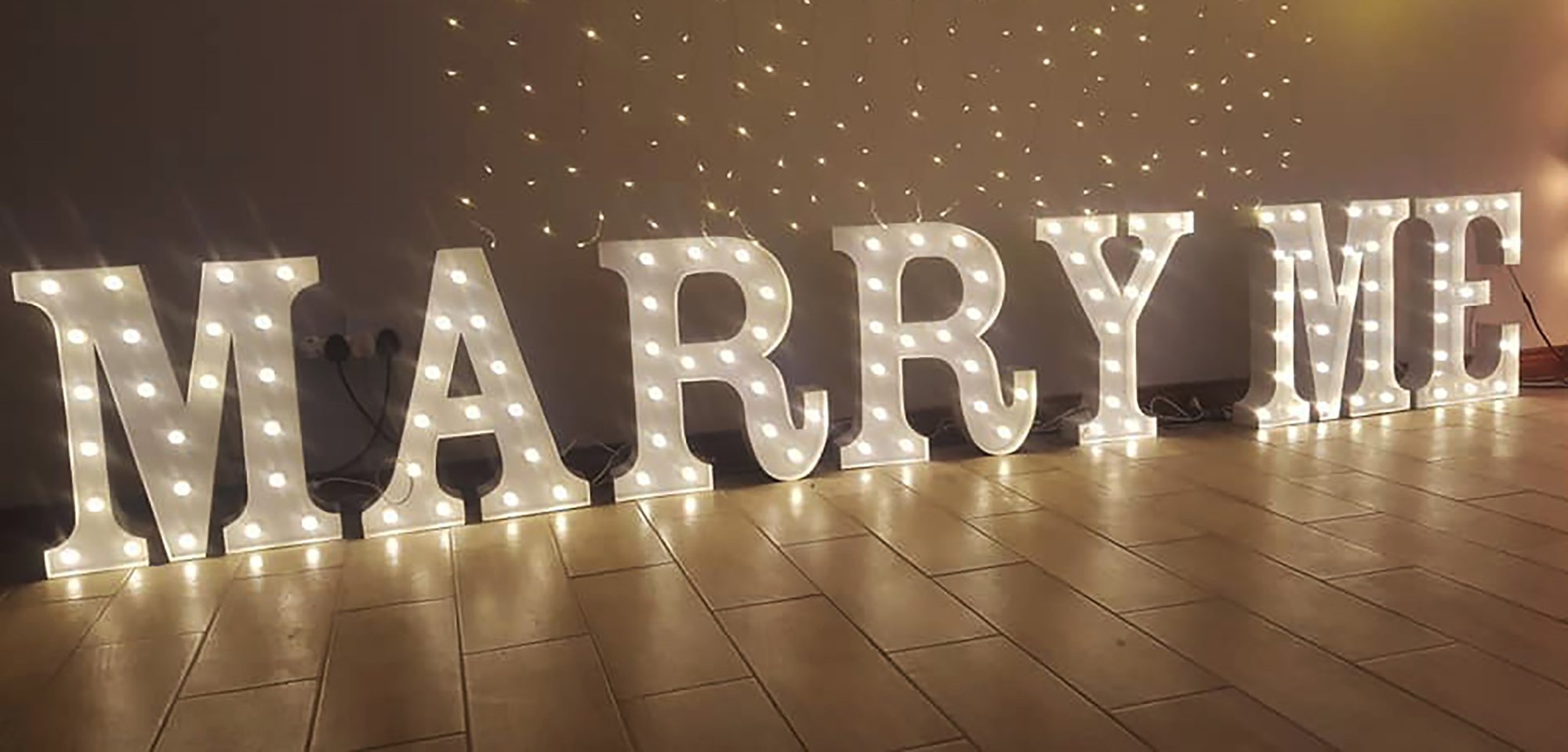 Brightly lit marquee letters spelling Marry Me