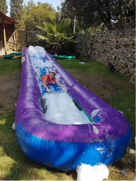 Person sliding down a purple foam water slide in a grassy area.