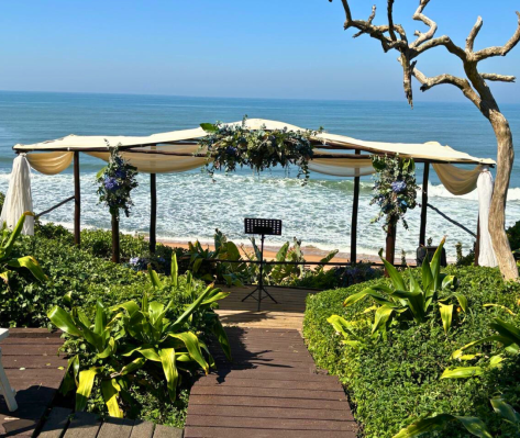 Beach wedding ceremony setup with ocean view and greenery.