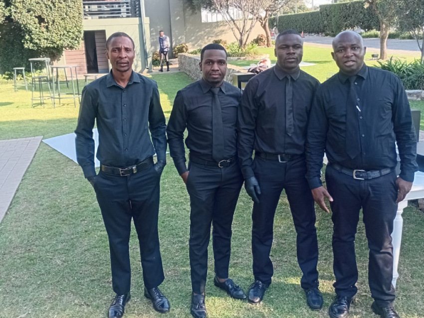 Four professional waiters in black attire on the lawn