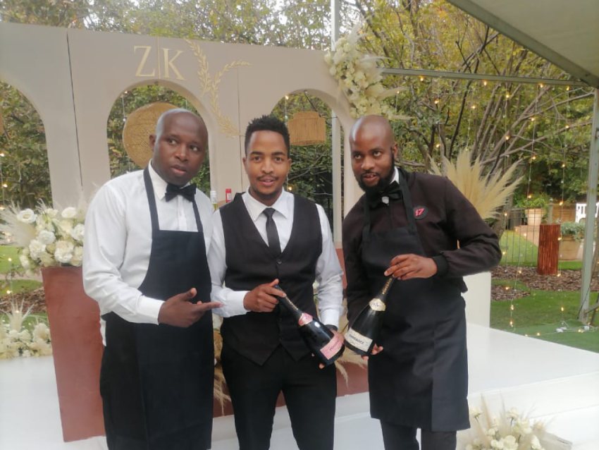 Three professional waiters presenting champagne bottles at an event