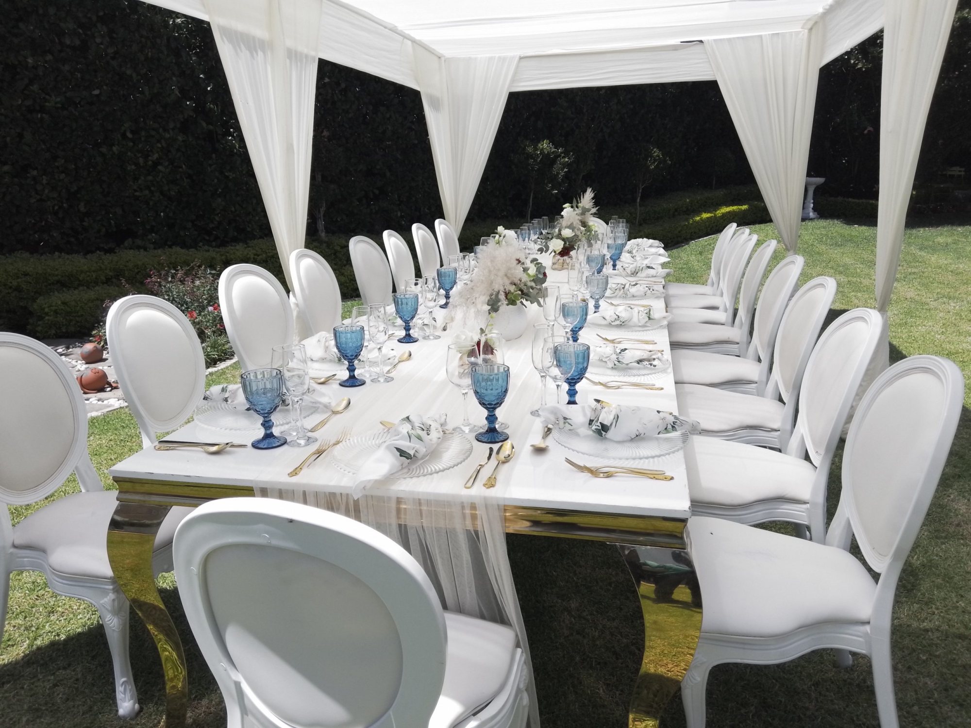 Outdoor dining table set with white chairs and blue glassware.