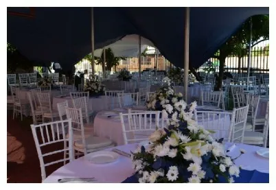 Seating arrangement with white chairs and floral centerpieces under a tent