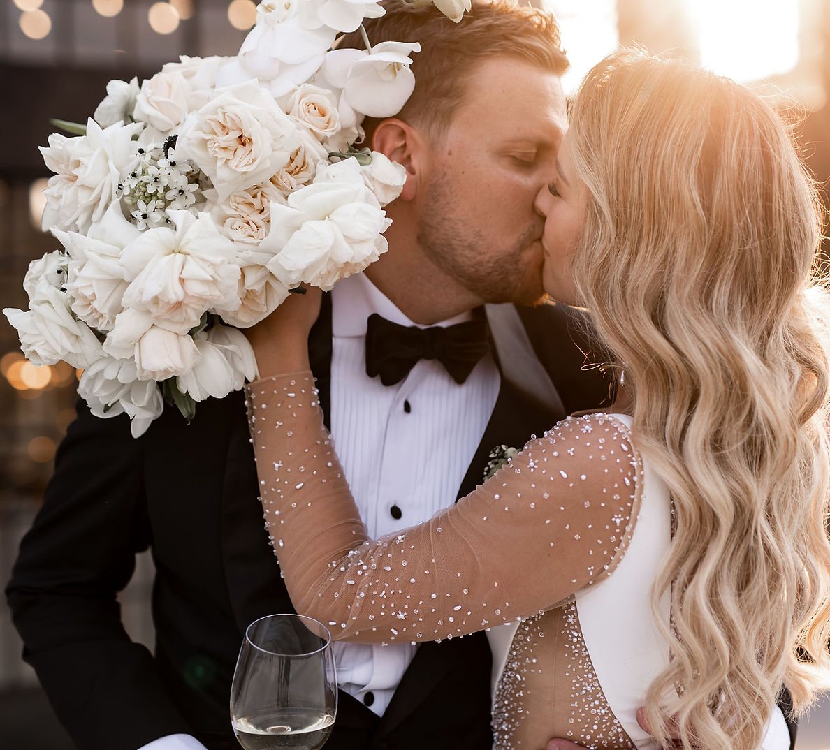 Bride and groom sharing a kiss at sunset with a floral bouquet
