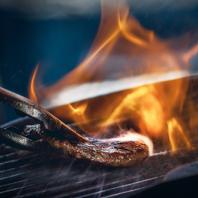 Close-up of steak grilling with flames and smoke