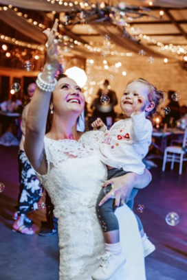 Bride holding a child amidst bubbles at a celebration