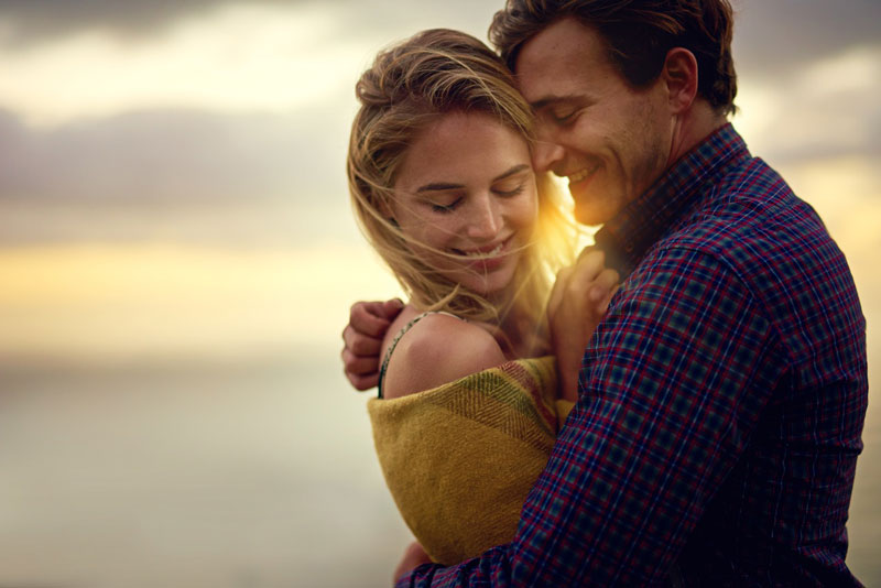 Couple embracing against a beach sunset backdrop